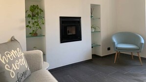 A living room with a fireplace, a sofa, a chair, and glass shelving with plants. - Spazio Perlasca apt1 - Cernobbio Como Lake (Cernobbio)
