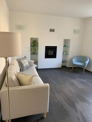 A living room with a sofa, a chair, a floor lamp, a fireplace, and shelves with decorative items. - Spazio Perlasca apt1 - Cernobbio Como Lake (Cernobbio)