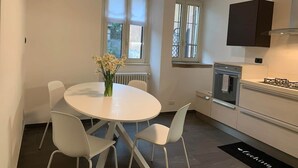A modern kitchen with white cabinetry, a built-in oven, and a gas stove. There is a round dining table with white chairs and a vase of flowers. - Spazio Perlasca apt1 - Cernobbio Como Lake (Cernobbio)