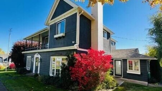 A two-story house with a dark exterior, a visible garage door, and a well-maintained lawn. - Wildflower Suites North (Garfield)