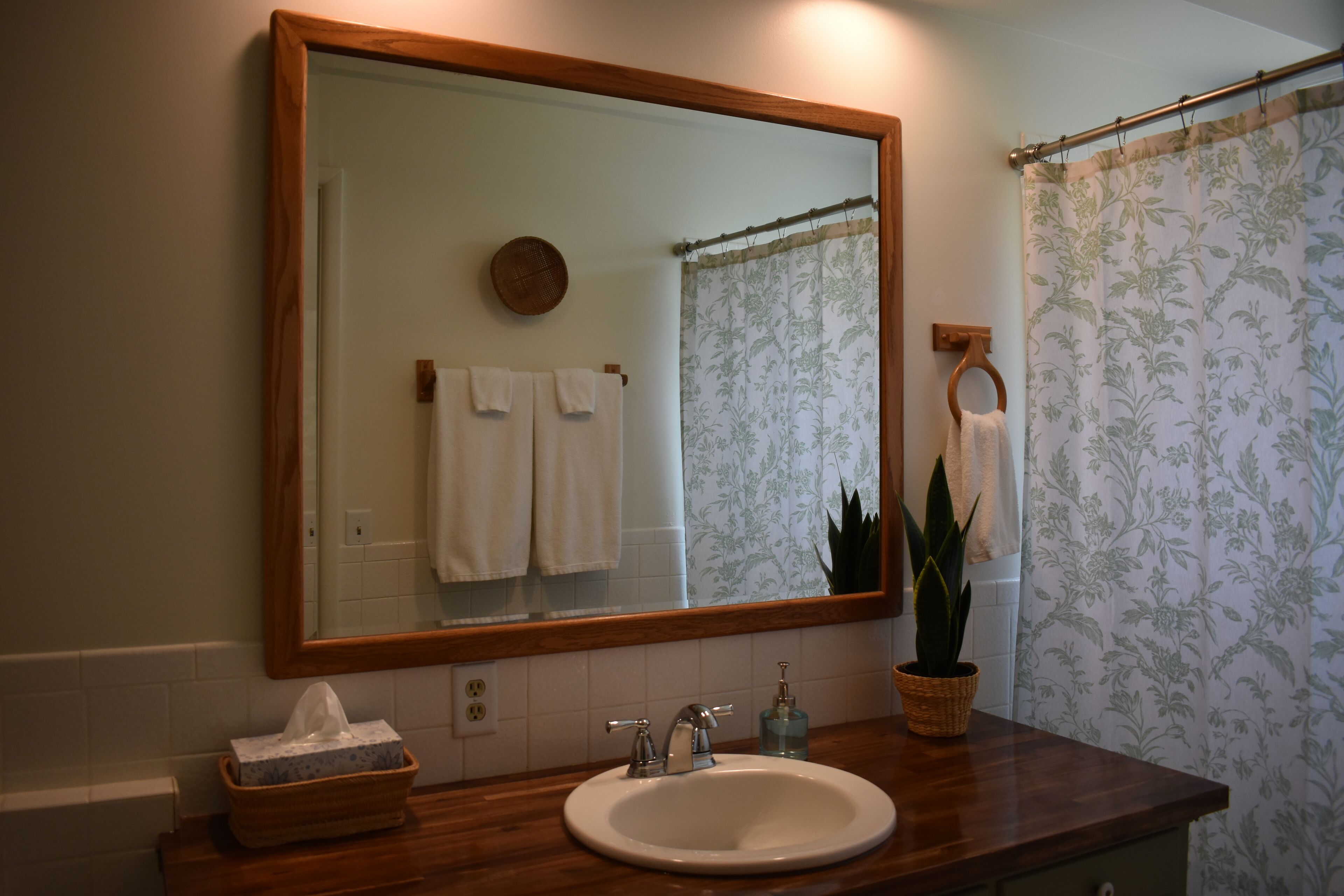 A bathroom with a wooden vanity, a white sink, a mirror, and a shower curtain.