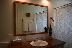 A bathroom with a wooden vanity, a white sink, a mirror, and a shower curtain. - Wildflower Suites North (Garfield)