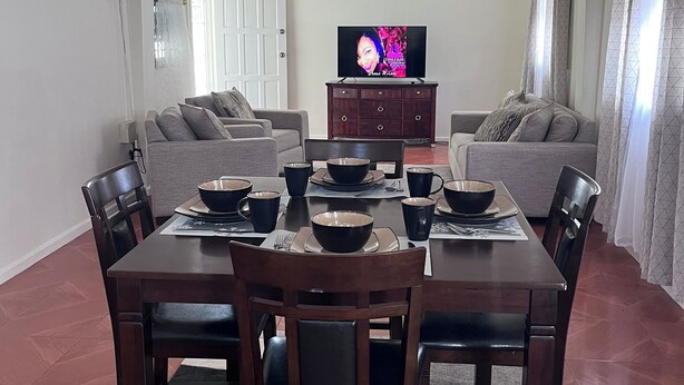A dining area with a rectangular table set for four, flanked by two sofas. A flat-screen TV is mounted on the wall above the sofa. - Charming 2-bedroom apartment with WiFi, AC in delightful Georgetown. (Georgetown)