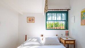 Un dormitorio con cama, una mesita de noche, una ventana con vista a palmeras y un cuadro en la pared.