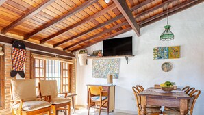 Un comedor amplio con mesas y sillas de madera, una pared de ladrillo con una obra de arte colorida, y un televisor montado en la pared.