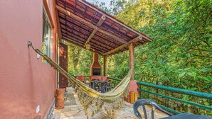 Una hamaca en un patio de piedra con una pérgola de madera, rodeada de abundante vegetación.