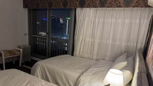 Camera d'albergo con due letti, vista notturna sulla città, un termosifone e una sedia.