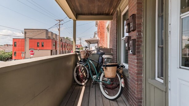 A balcony with a bicycle and a basket, overlooking a street with buildings.