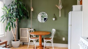 A dining area with a round wooden table and two white chairs, a potted plant, a wall-mounted mirror, and a white refrigerator.
