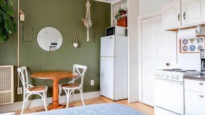 A compact kitchen with white appliances, a dining table with chairs, and a hanging plant.