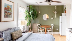 A bedroom with a bed, a desk, a chair, a dining table, and a plant.
