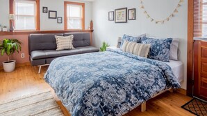 Ein Schlafzimmer mit Bett, Sofa, Zimmerpflanze und gerahmten Bildern an der Wand.