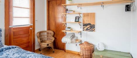 Ein Schlafzimmer mit einem Bett, einem Sessel, einer Holztür, einem Regal mit Dekoration und einem grünen Truhenkasten.