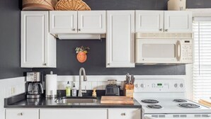 A kitchen with white cabinets, a stainless steel sink, a microwave, a stove, and a toaster.