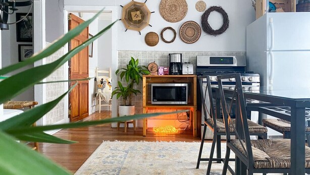 A cozy kitchen with a dining area, featuring a wooden table, chairs, and a variety of decorative items on the wall.