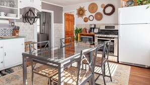 A modern kitchen with a glass dining table, stainless steel appliances, and decorative wall hangings. - Bohemian Penthouse | 1min Walk Restaurants + Shops (Winooski)