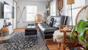 A living room with a black leather sofa, a wooden chair, a patterned rug, and a television on the wall. - Bohemian Penthouse | 1min Walk Restaurants + Shops (Winooski)