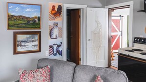 A living room with a grey sofa, a painting of a rooster, a painting of a cat, and a painting of a cow. - Historic Farmhouse Apartment (Fairfield)