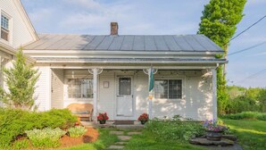 A white house with a porch, a front door, and a small garden with plants and stepping stones. - Historic Farmhouse Apartment (Fairfield)