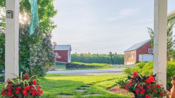 A rural landscape with a barn, a small red structure, and potted red flowers in the foreground. - Historic Farmhouse Apartment (Fairfield)