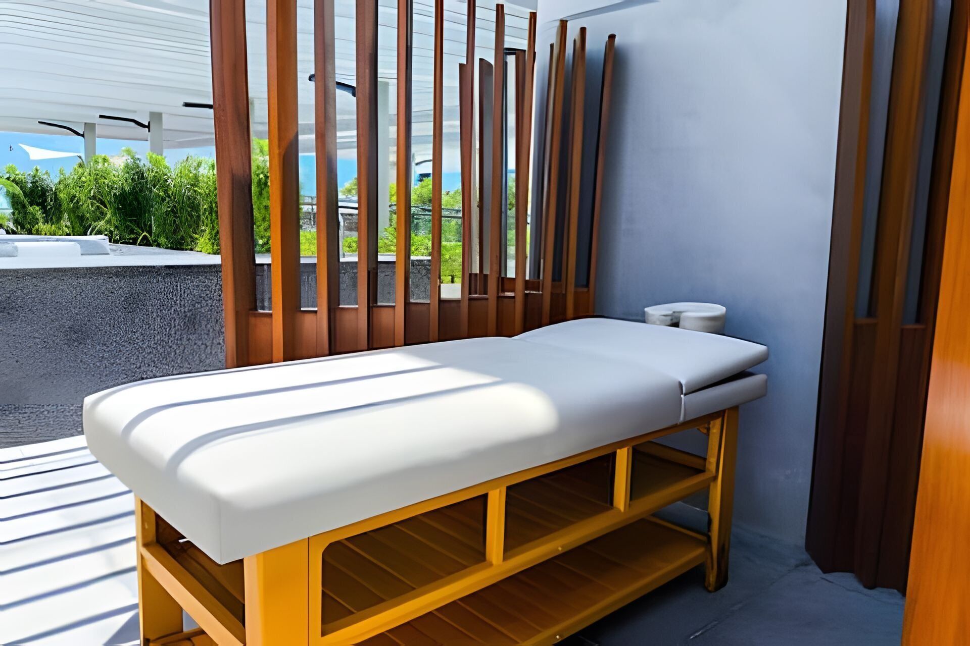 A modern massage table with a white mattress, wooden frame, and a small shelf underneath.