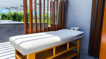 A modern massage table with a white mattress, wooden frame, and a small shelf underneath.
