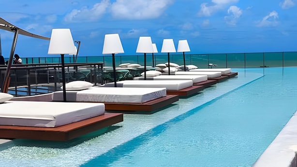 A poolside area with multiple sun loungers and umbrellas, a glass railing, and a clear view of the ocean. - Setai Yacht (João Pessoa)