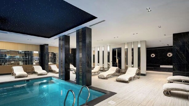 Un área de piscina interior moderna con sillones de descanso y un techo con estrellas.