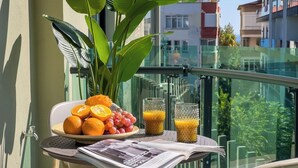 Un balcón con una mesa preparada para el desayuno, que incluye frutas, vasos de jugo y un periódico.