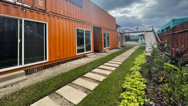 A modern house with a large sliding door, a small deck, and a garden with various plants. - Container Project  (Puerto Morelos)