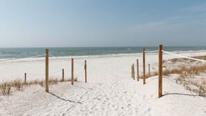 Une plage de sable avec des poteaux et des cordes en bois, qui mènent à l’océan.
