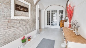 A hallway with a brick wall, a white-framed sign, a wooden bench, and a door with glass panels. - AriediParma - Rooms & Apartments (Parma)