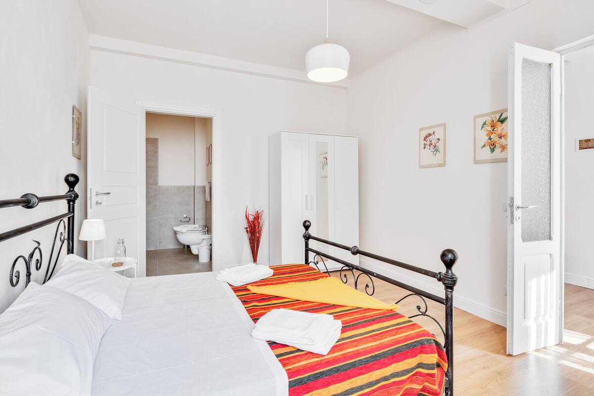 A bedroom with a bed, a wardrobe, a bathroom, and a door leading to another room.