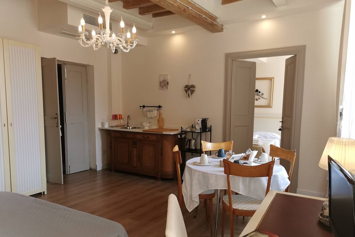A dining area with a table set for two, a chandelier, and a kitchen in the background.