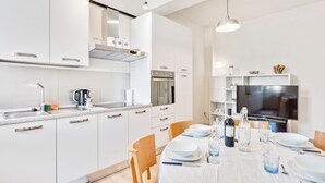 A modern kitchen with white cabinets, a built-in oven, and a dining area set for six with a white tablecloth and plates. - AriediParma - Rooms & Apartments (Parma)