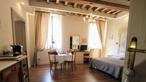 A hotel room with a wooden floor, a bed, a desk with a computer, a chair, a dining table with chairs, and a chandelier. - AriediParma - Rooms & Apartments (Parma)