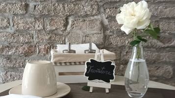 Una tavola apparecchiata con un teiera bianca, una tazza bianca, un piatto bianco, un tovagliolo bianco e un vaso trasparente con un fiore bianco, oltre a una lavagna con la scritta 'Triviatore'.