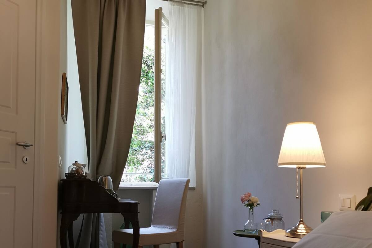 A hotel room with a bed, a desk with a chair, a lamp, and a window with curtains.