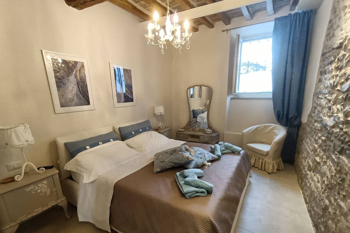 A bedroom with a large bed, a nightstand, a dresser, a chair, a mirror, and artwork on the walls.