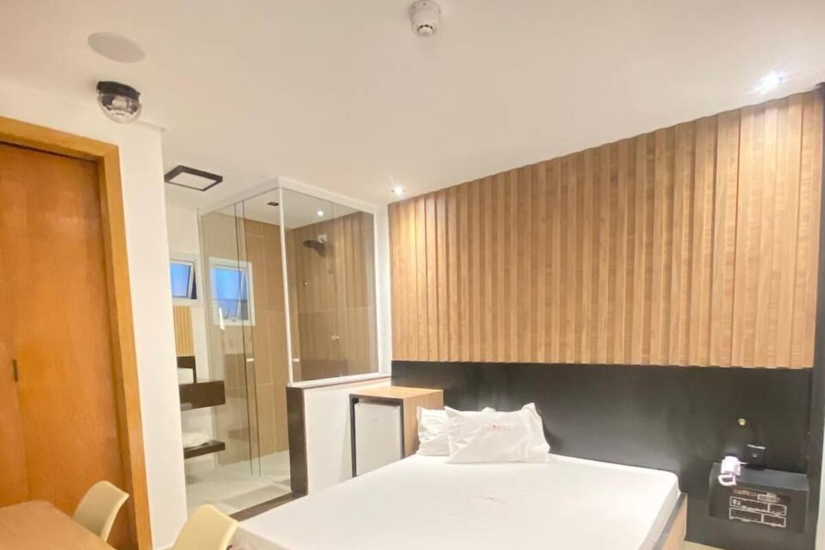 Moderni hotellihuone, jossa on suuri sänky, työpöytä ja tuoli. Huoneessa on peili ja puupanelilla verhoiltu seinä.