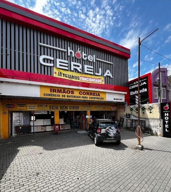 A hotel named 'Hotel Cereja' with a signboard advertising 'IRMAOS CORREIA' and 'CEMÉRIO DE MATERIAIS PARA CONSTRUÇÃO'.