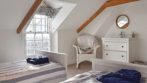 Une chambre avec deux lits, une chaise, une commode et une fenêtre avec des rideaux.