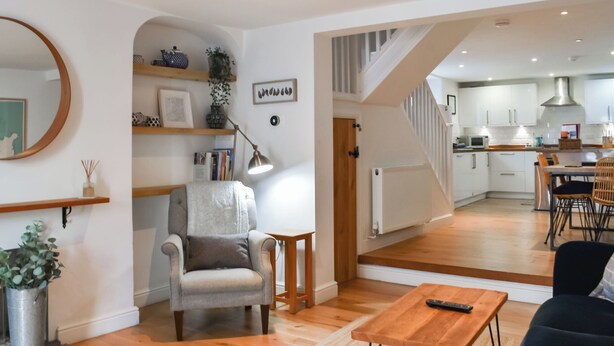 Un salon moderne avec un canapé, une table basse et un fauteuil. Un escalier mène à un espace cuisine comprenant une table à manger et des chaises.