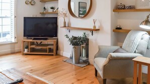 Un salon avec un téléviseur, des étagères en bois, un miroir et un fauteuil gris.