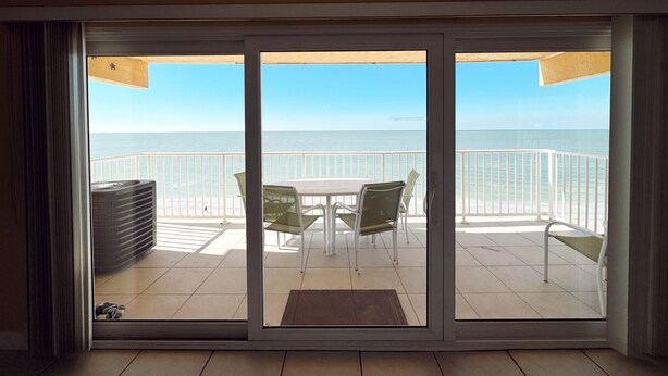 A balcony with a view of the ocean, a table, chairs, and a small seating area.