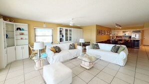 A spacious living area with a white sofa set, a glass coffee table, and a white cabinet.