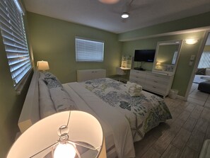 Un dormitorio con cama, mesitas de noche, escritorio, silla, televisor y espejo.