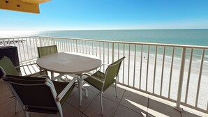 A balcony with a round table and chairs, overlooking a beach with a clear view of the ocean.