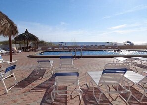 A pool area with lounge chairs and a view of the ocean.