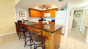 A kitchen with wooden cabinets, a central island with bar stools, a ceiling fan, and a microwave.